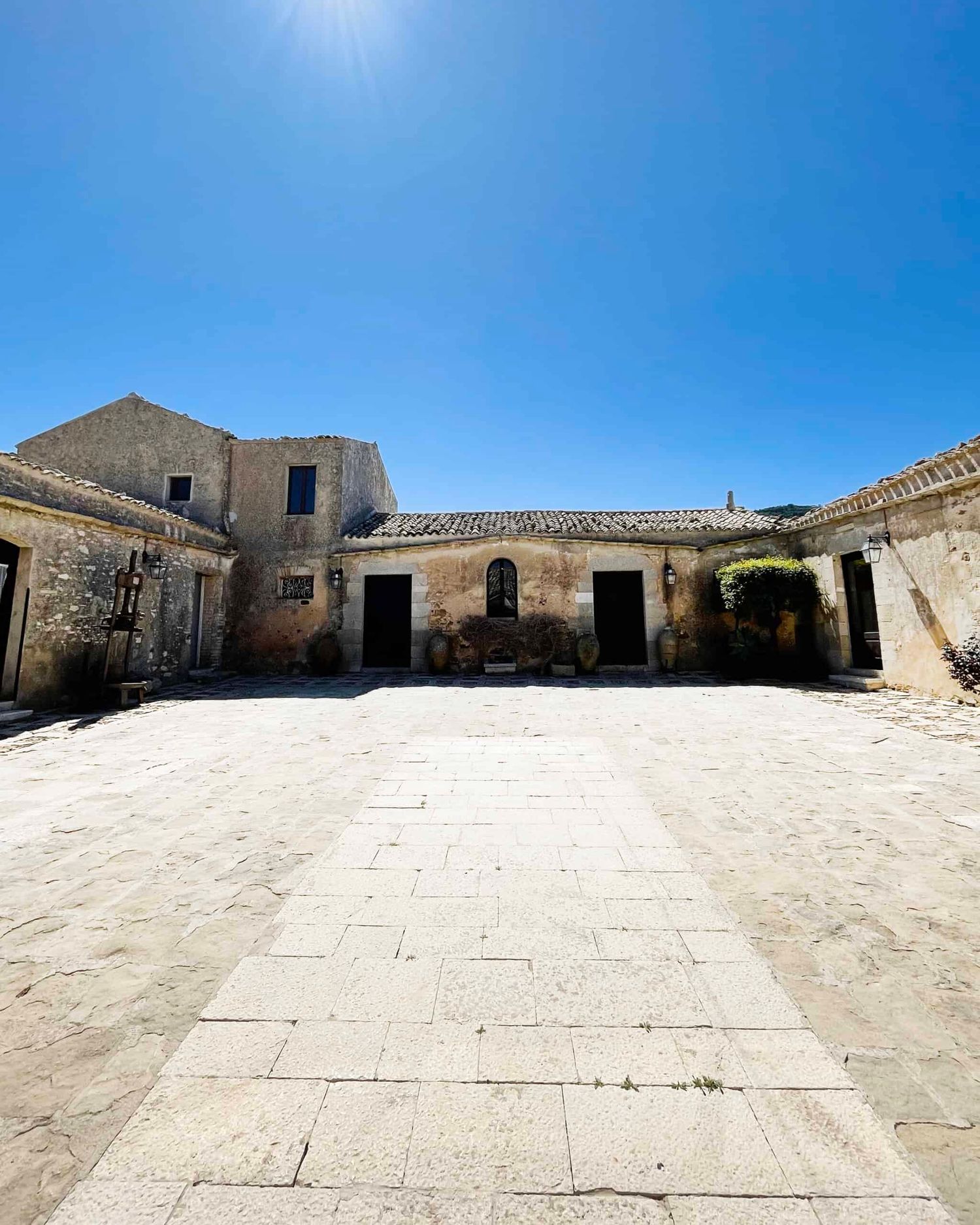 Historic stone farmhouse courtyard with arched doorways and terracotta pots in sunlight.