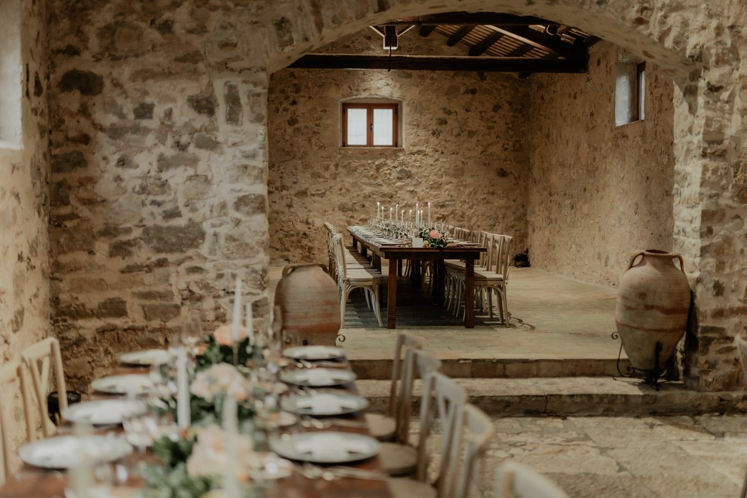 Rustic stone barn wedding venue with long dining tables set for reception, featuring elegant place settings and soft candlelight.