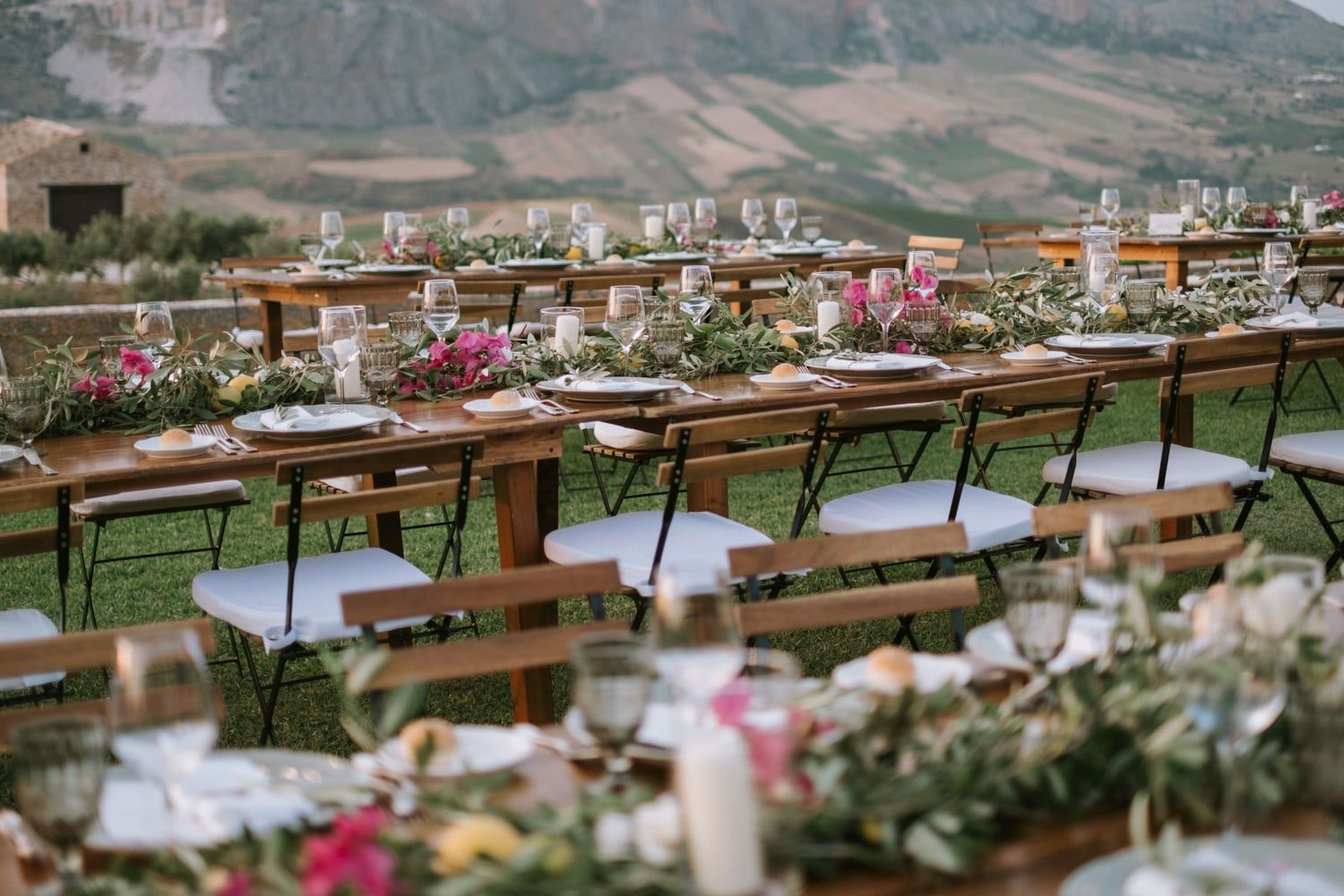 Elegant outdoor wedding reception with long wooden tables, floral centerpieces, and scenic mountain views.