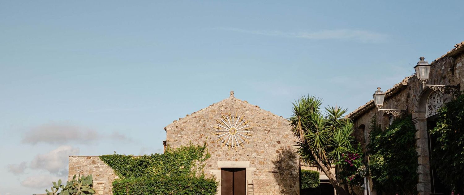 Historic stone church facade with rose window, palm trees, and ivy under a clear blue sky.