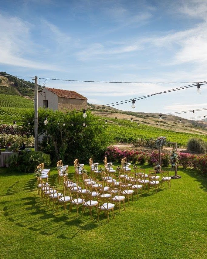 Outdoor wedding ceremony setup with gold chairs on green lawn surrounded by lush vineyard landscape.