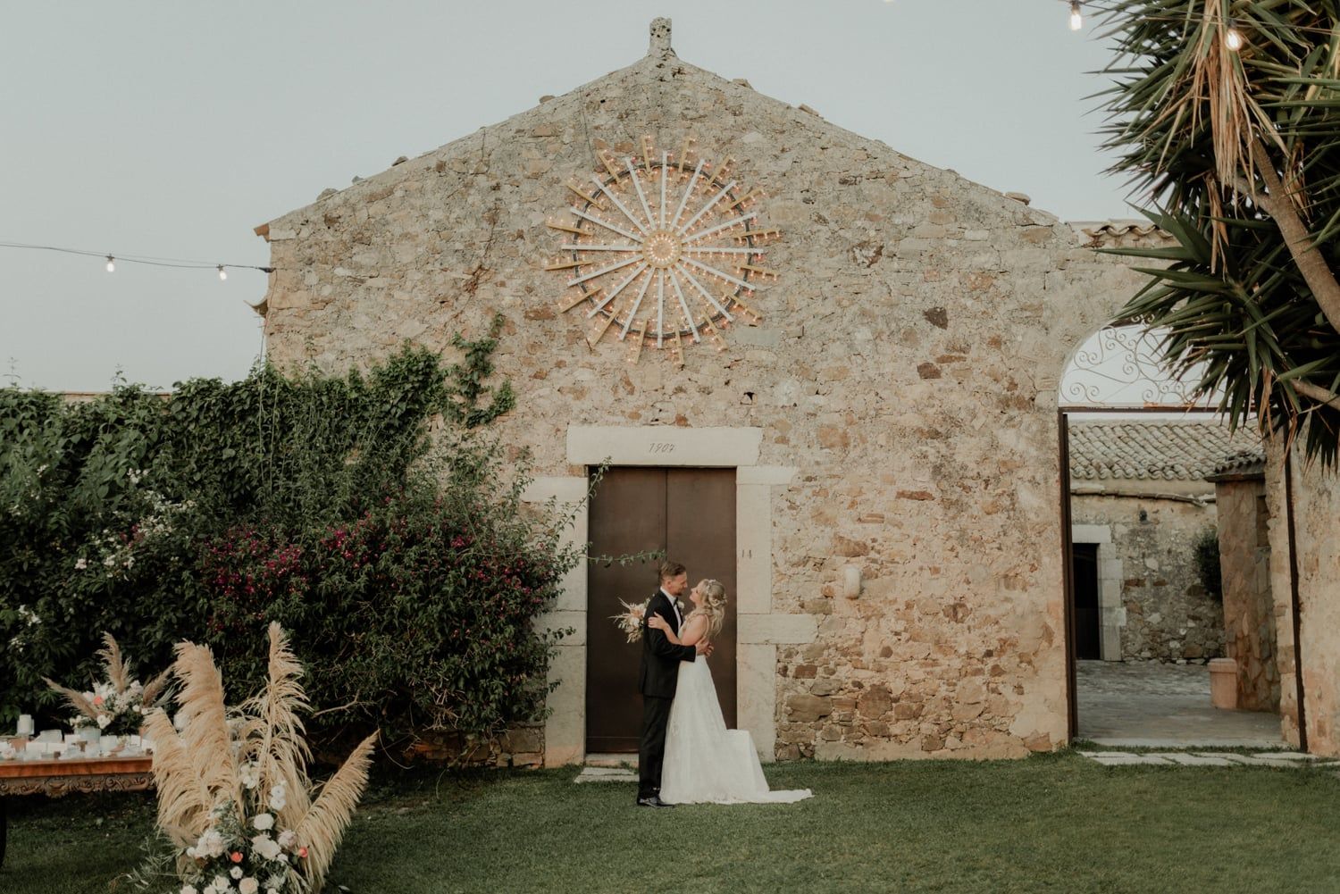 Bride and groom sharing a kiss outside a historic stone chapel with a rose window.