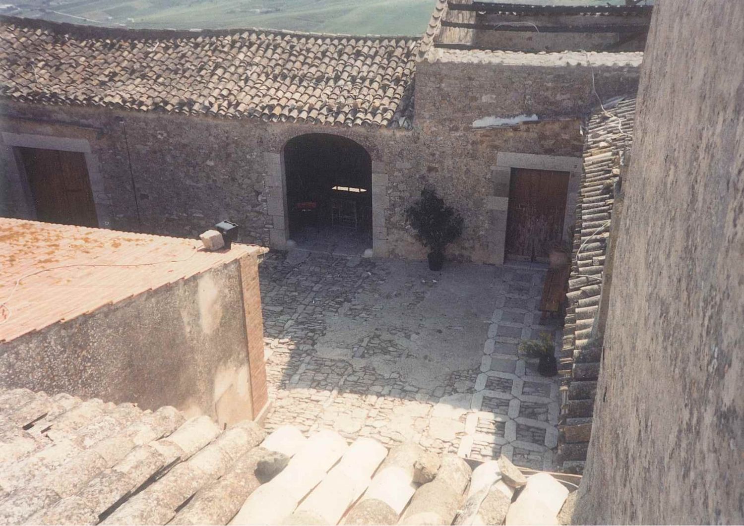 Aerial view of ancient stone courtyard with arched doorways and weathered brick flooring.