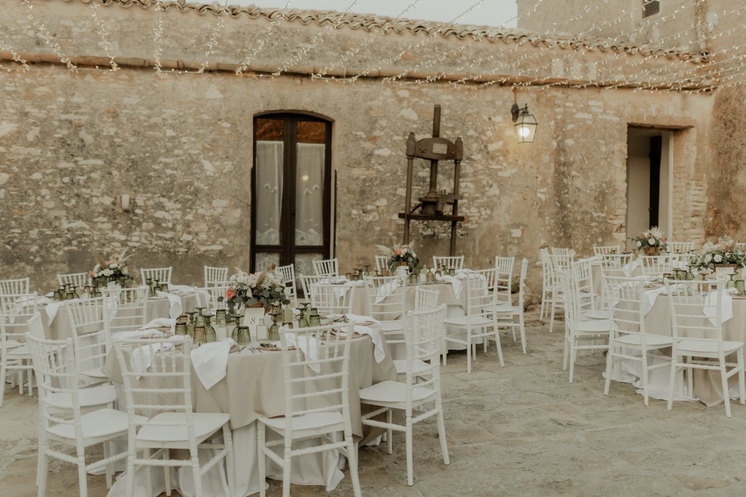 Elegant outdoor courtyard wedding reception with round tables and white chiavari chairs.