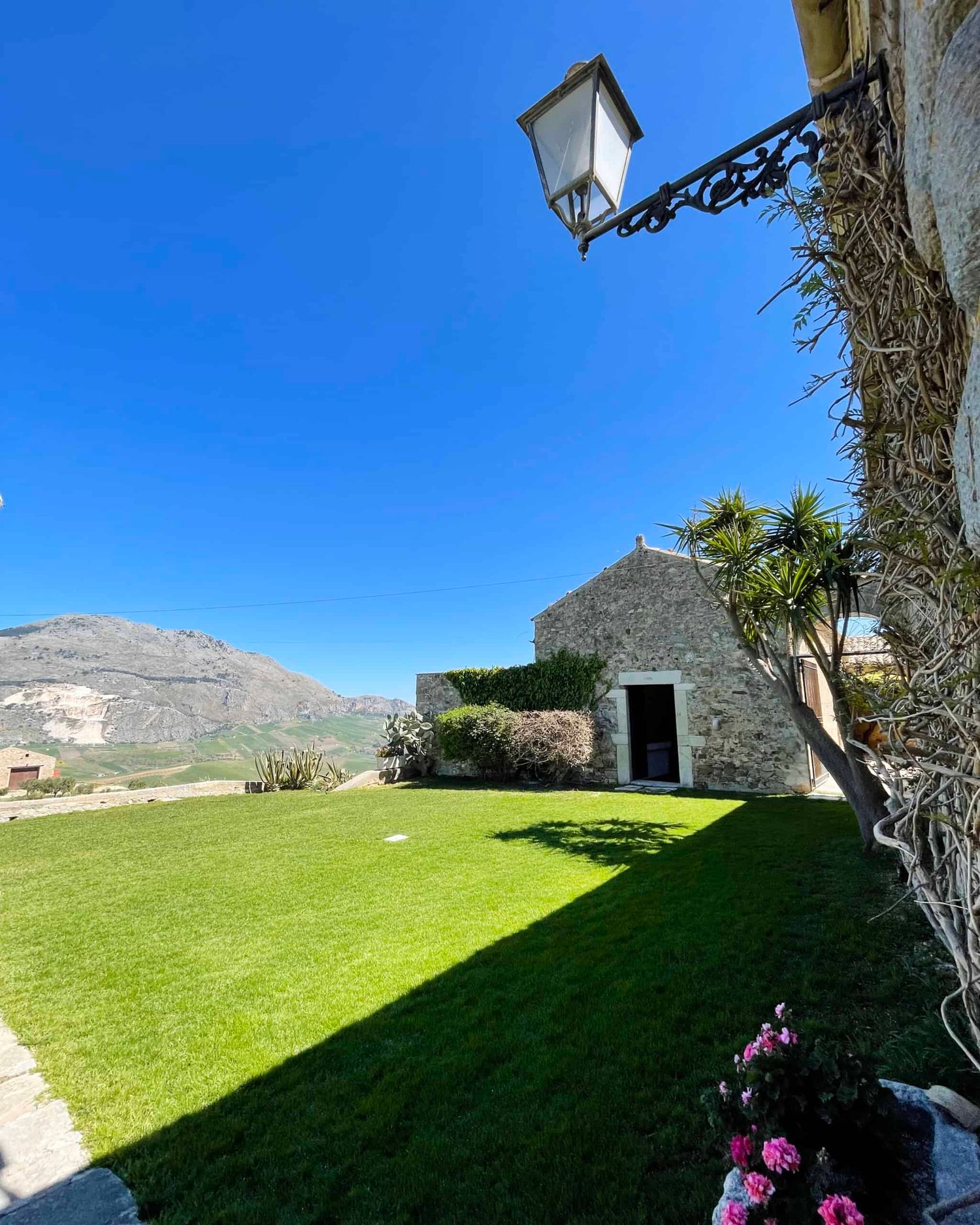 Stone building with ornate lamp, green lawn, and mountain backdrop under clear blue sky.