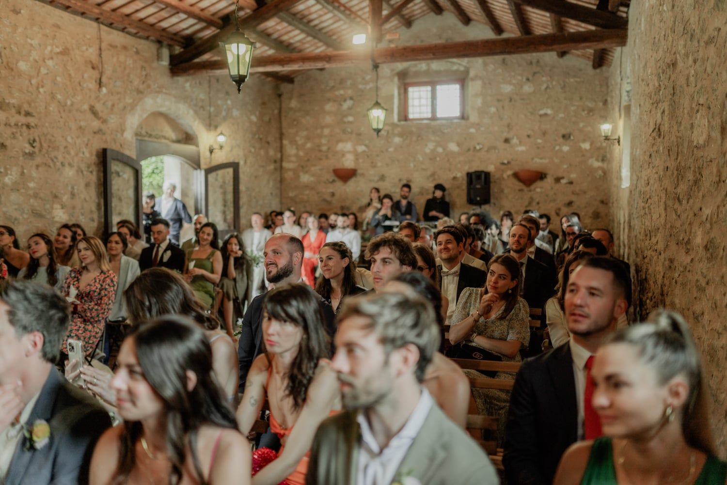 Guests fill rustic stone chapel wedding venue with wooden beams and arched doorways during an intimate ceremony.
