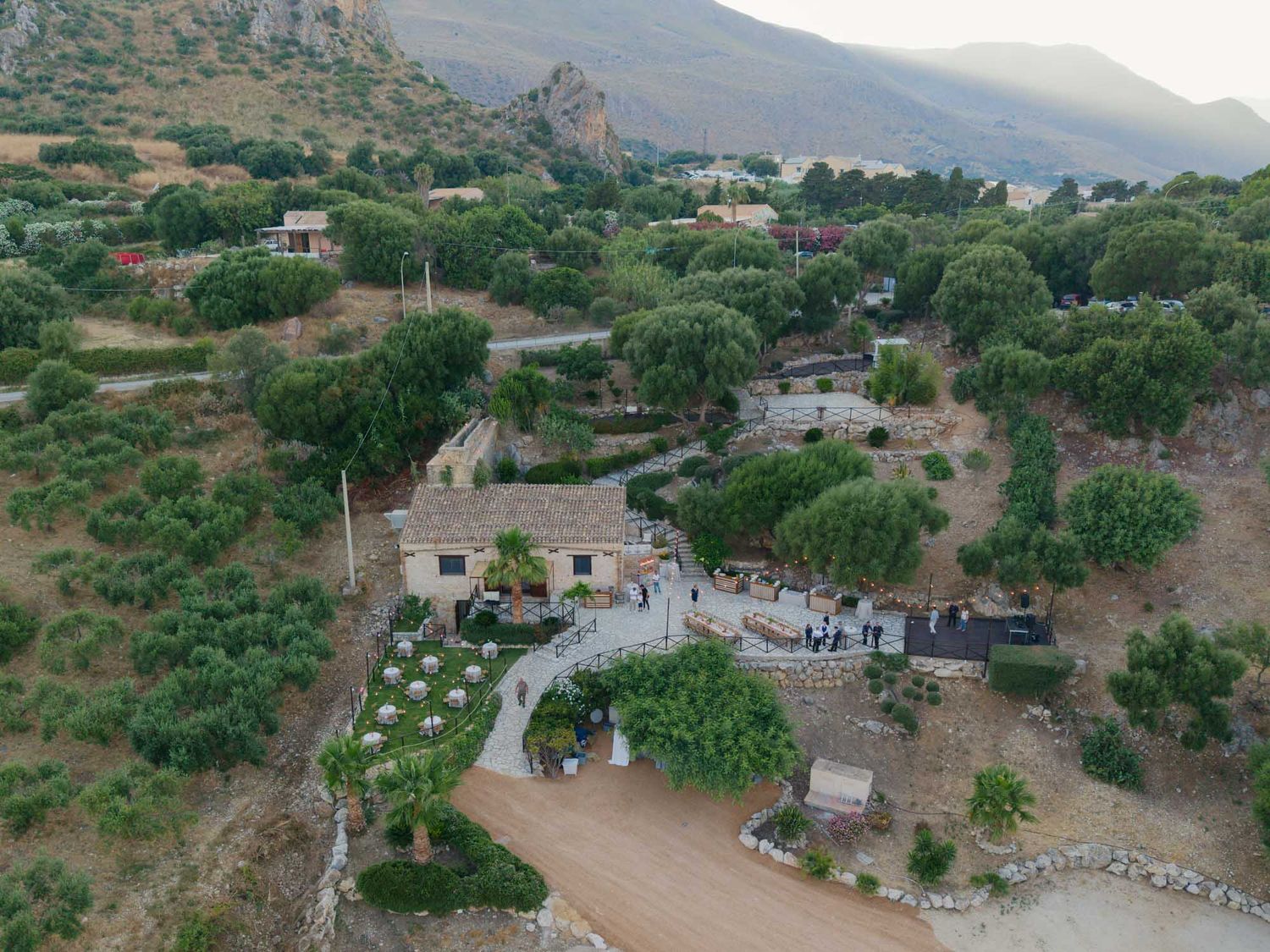 Aerial view of a rustic Mediterranean estate surrounded by olive trees and rocky hills at dusk.
