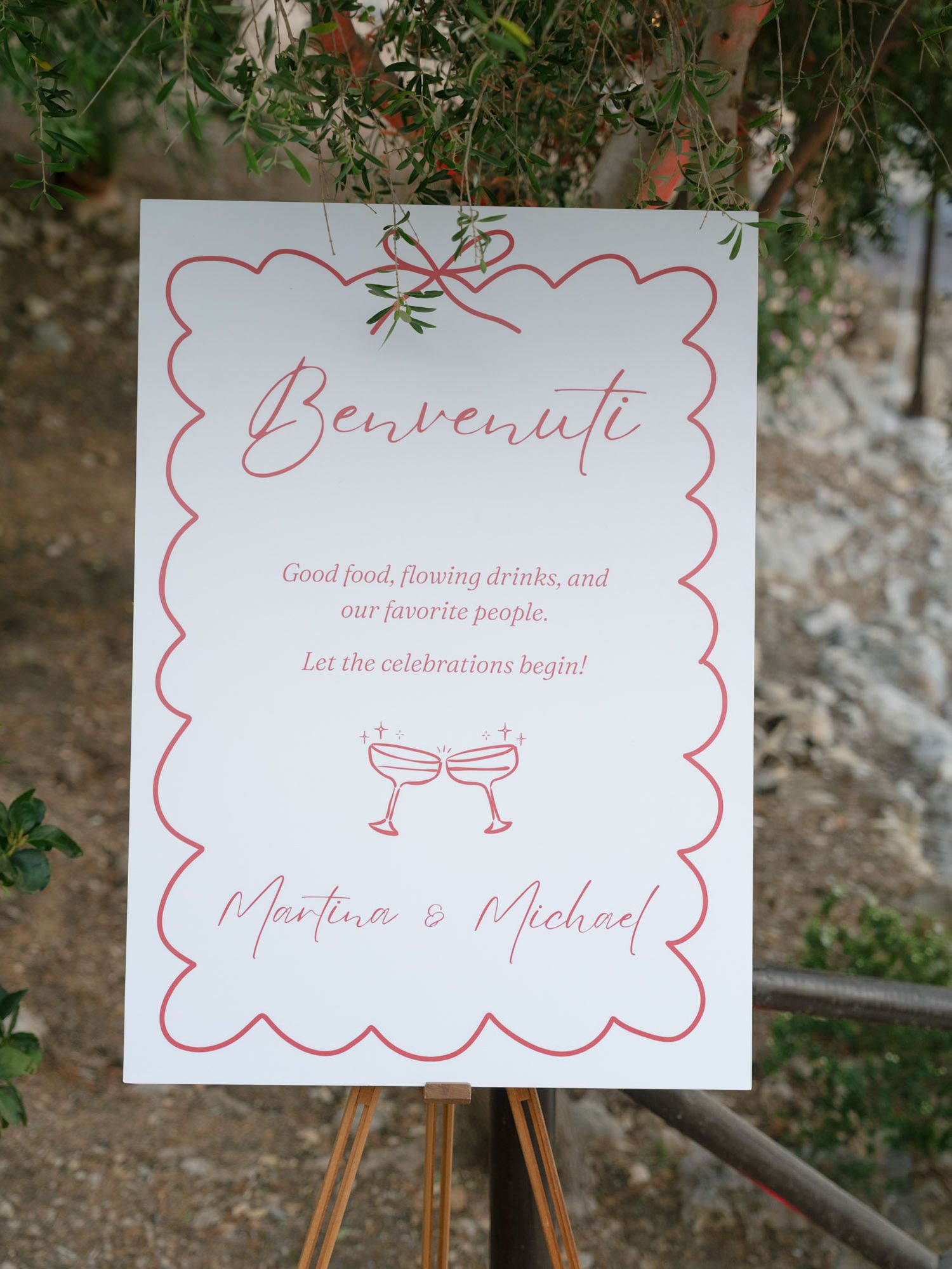 Wedding welcome sign on easel reading Benvenuti for Martina and Michael with red scalloped border and champagne glasses. Scopello, Sicily.