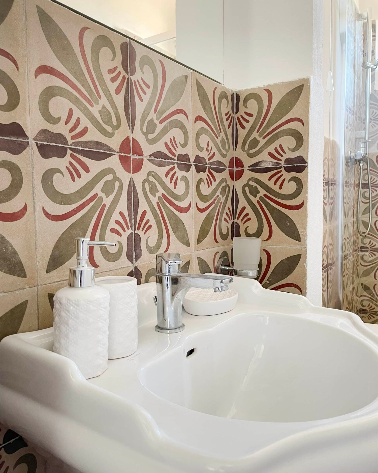 Stylish bathroom sink with decorative floral patterned tiles in red and green tones as a backsplash.
