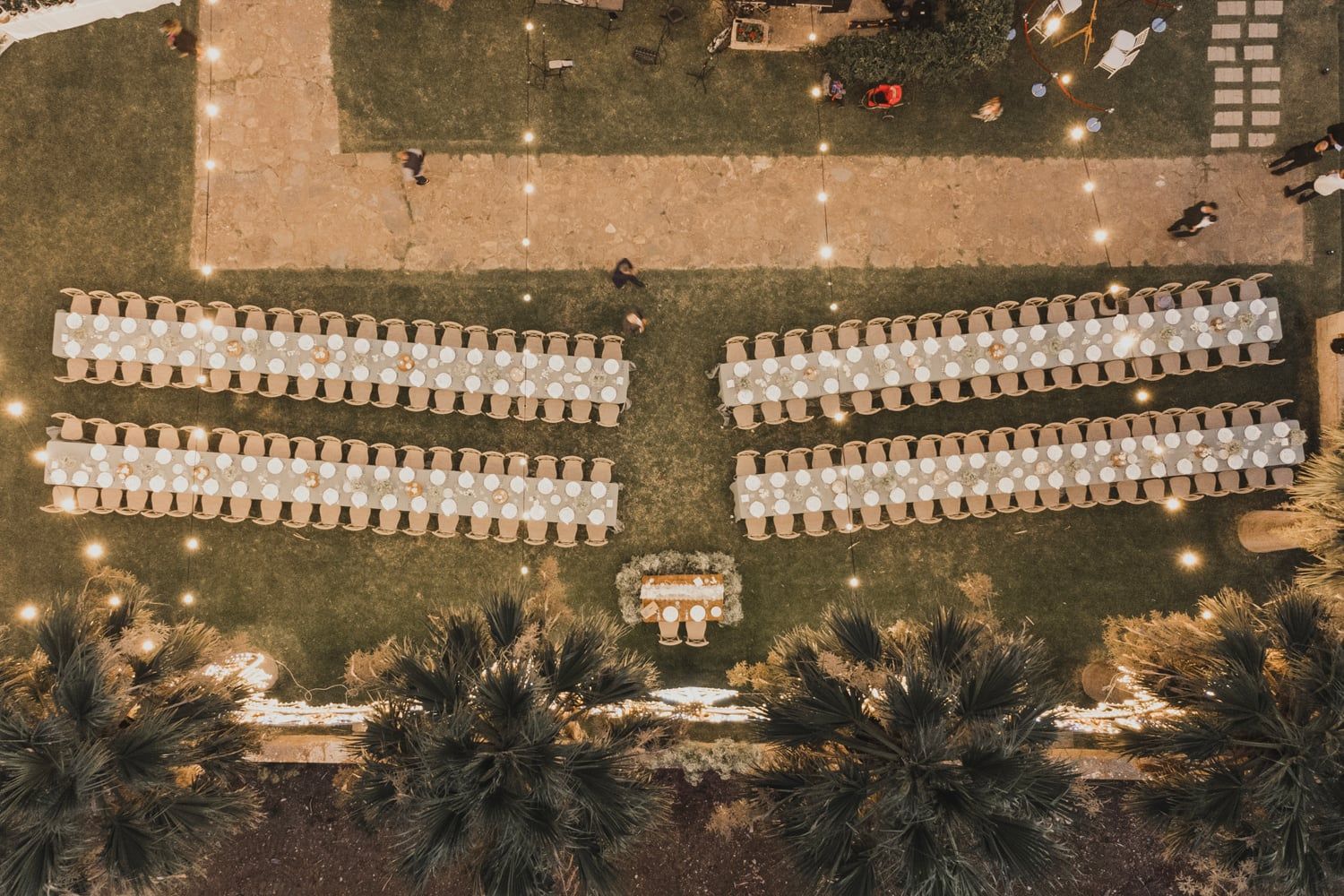 Aerial view of an elegant outdoor wedding ceremony setup with rows of white chairs on green lawn at dusk.