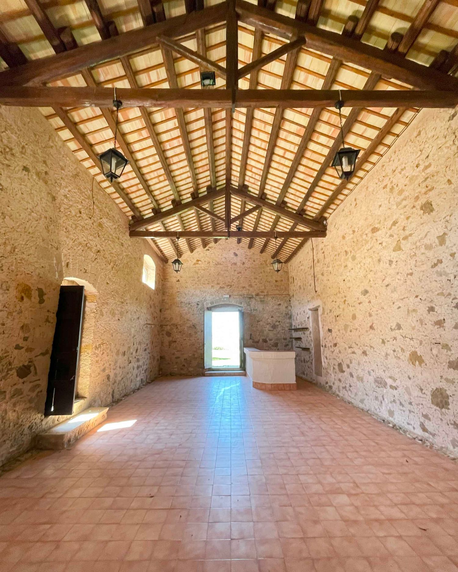Renovated stone building interior with wooden beam ceiling, terracotta tiles, and green door.