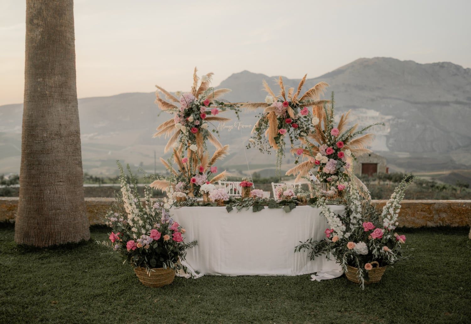 Elegant outdoor wedding sweetheart table with floral arrangements and mountain backdrop at sunset.