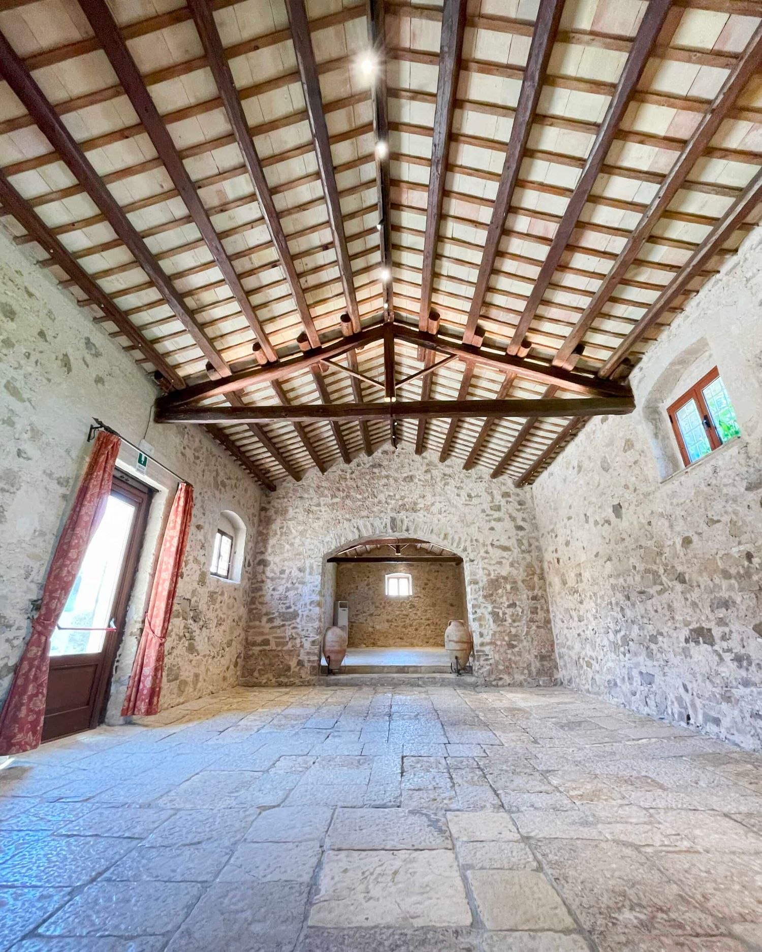 Rustic stone interior with wooden beam ceiling, arched alcove, and stone tile flooring.