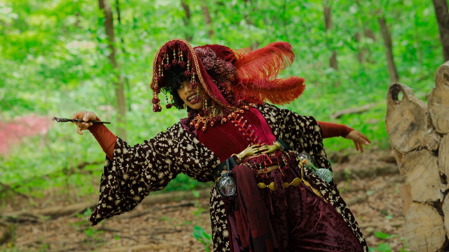 A performer in vibrant red and leopard print costume dances gracefully in a lush green forest setting.
