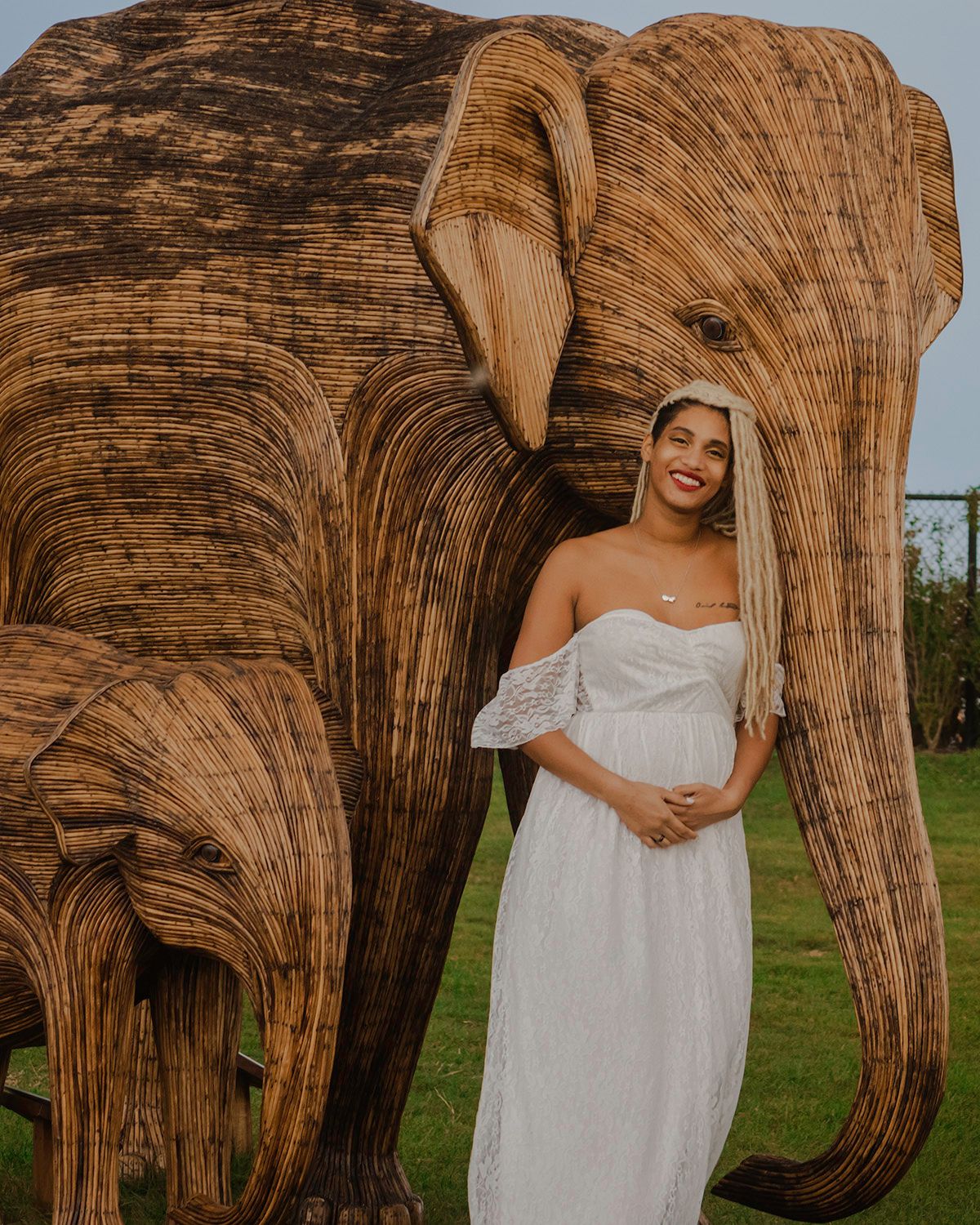 Maternity photos taken beside a large wooden sculpture in natural lighting.