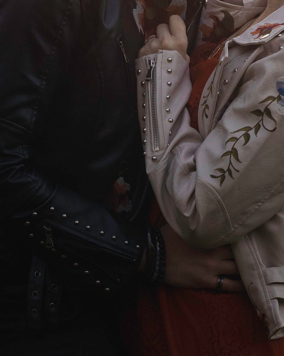 Close-up of two people in stylish jackets, one black studded and one white embroidered, standing close.