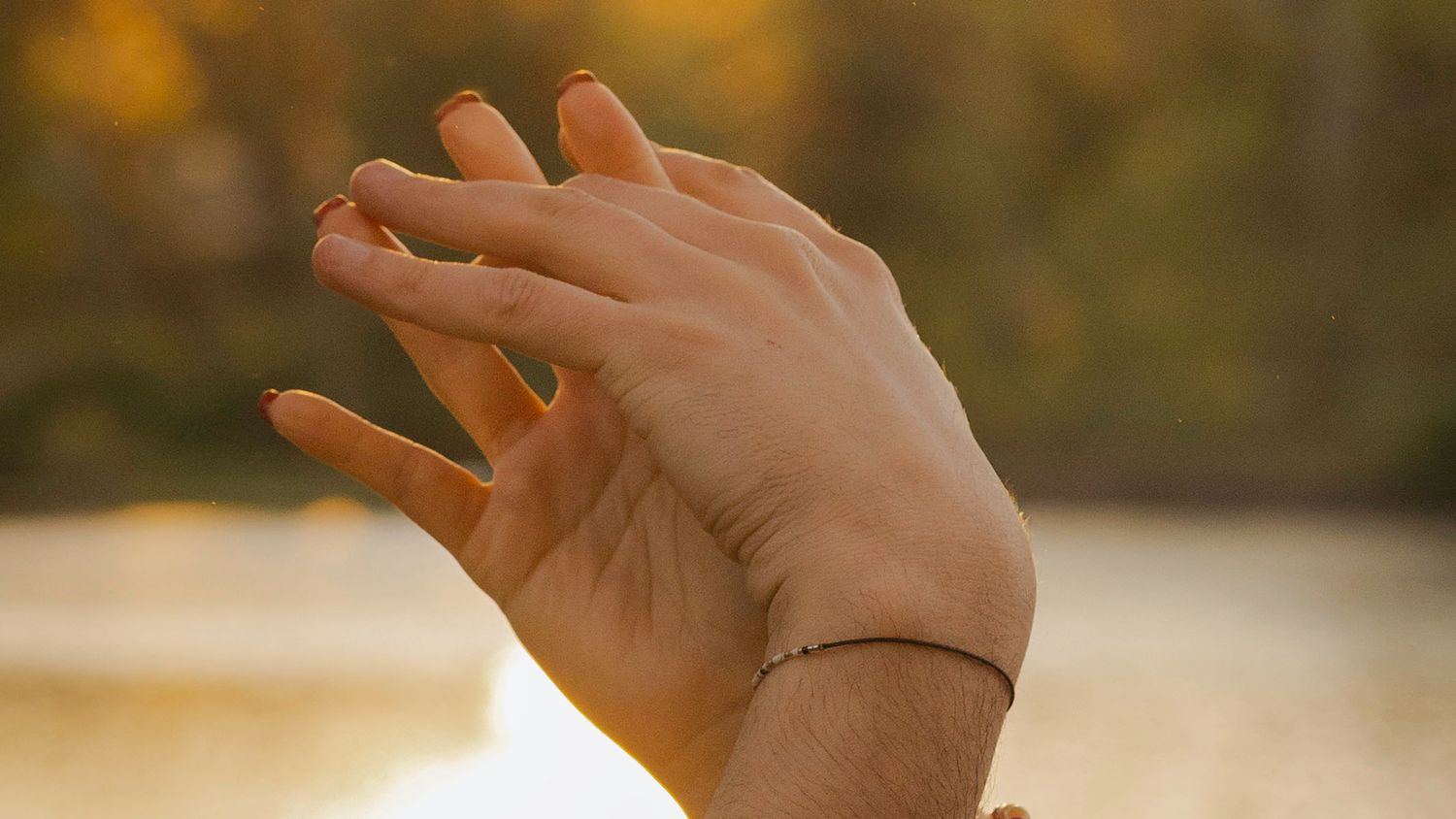 Close-up of two hands gently touching with a delicate bracelet in warm golden sunset light.