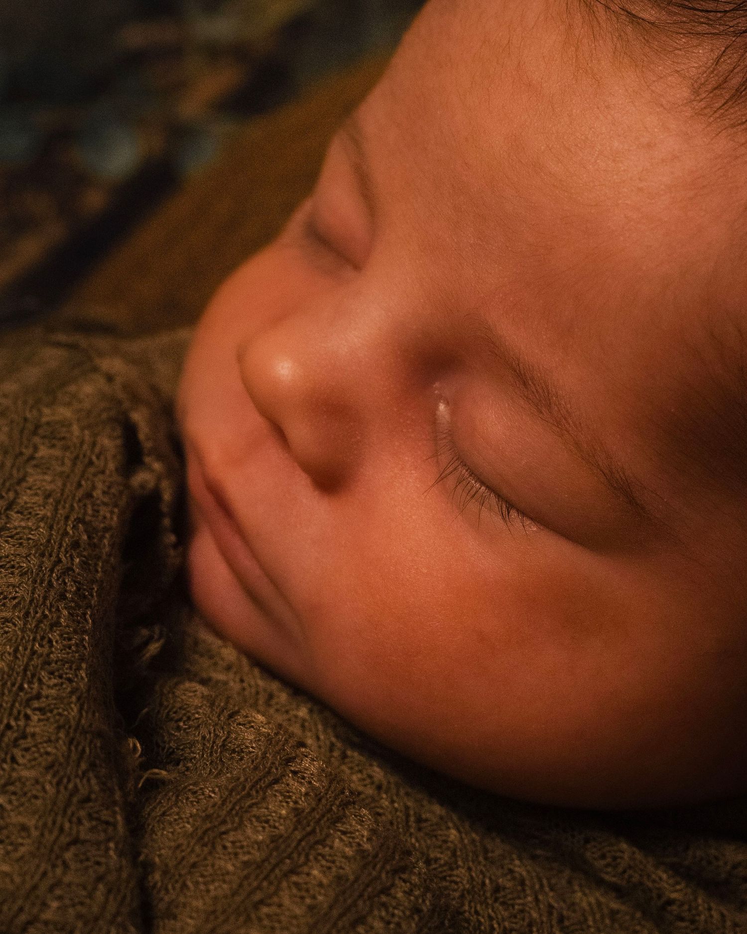 A series of close-up profile shots showing a sleeping infant's face in warm lighting against a textured background.