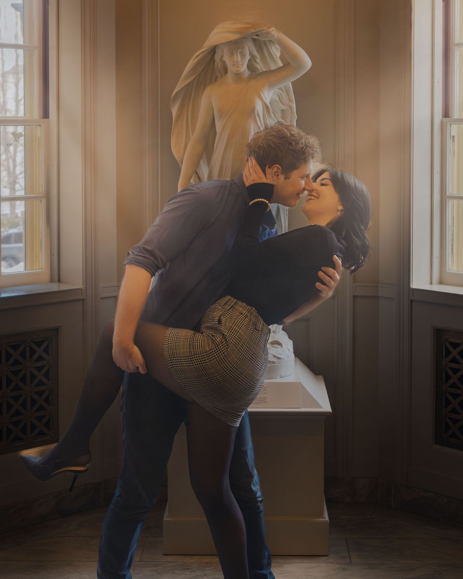 Couple sharing a romantic dip kiss in front of a classical marble statue in an elegant interior.