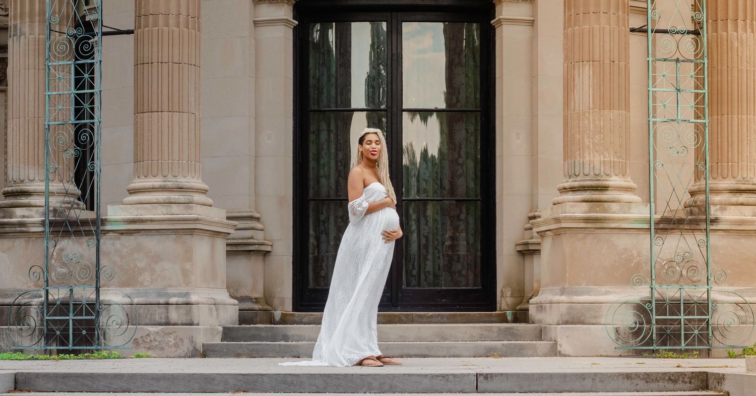 Classic architectural columns frame a maternity photo session on stone steps.