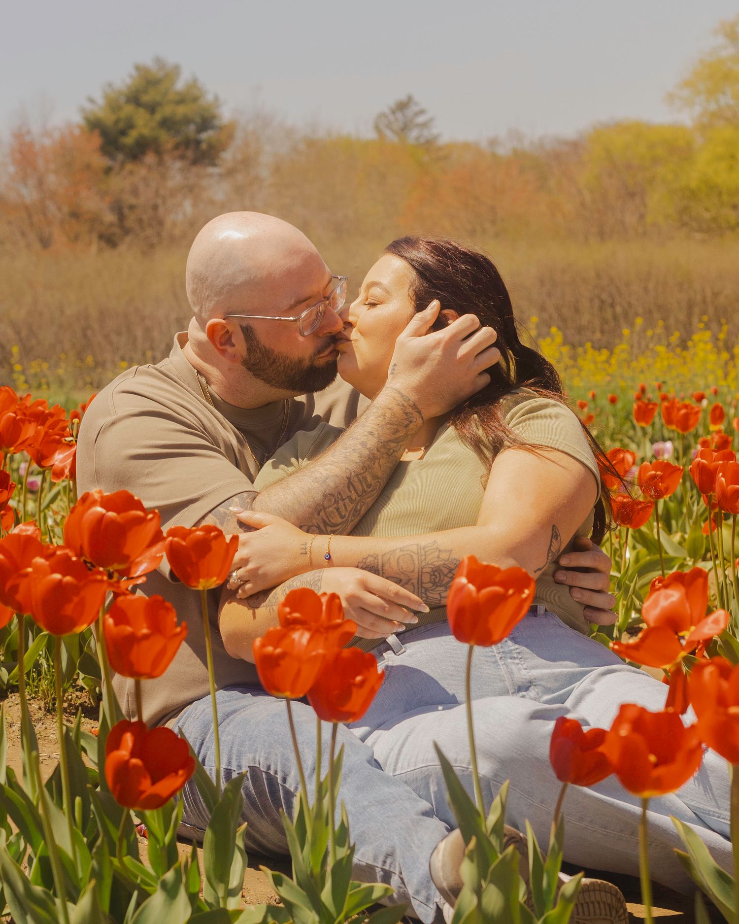 Couple kissing romantically among vibrant red tulips in a sunny spring garden field.