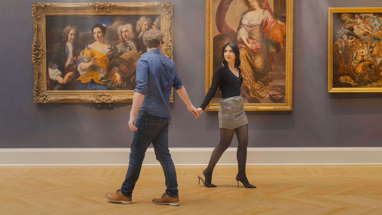 Couple holding hands in an art museum gallery surrounded by classical oil paintings on display.