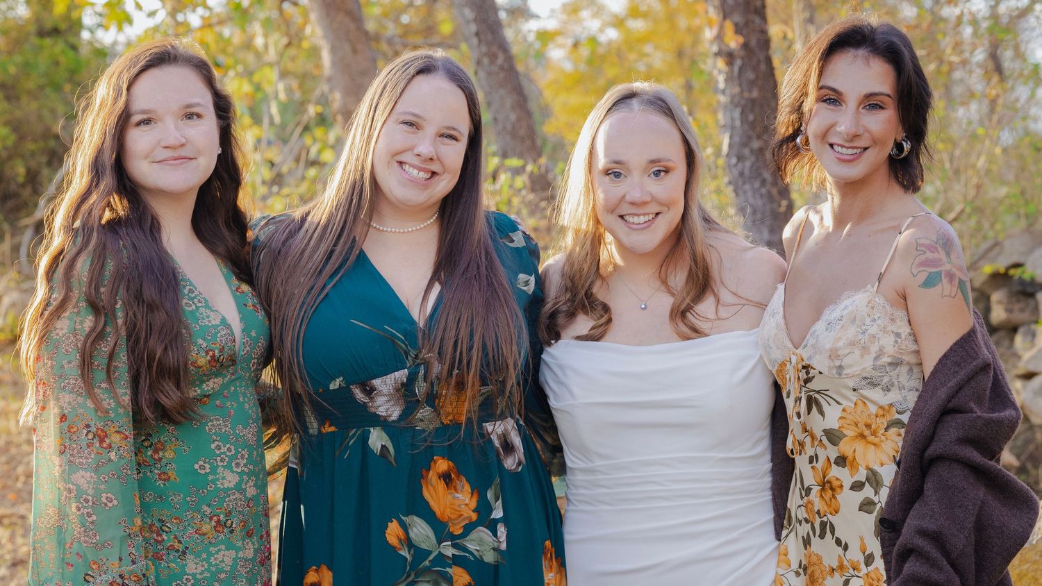 Group portrait of wedding party members wearing autumn-colored dresses against a natural backdrop.
