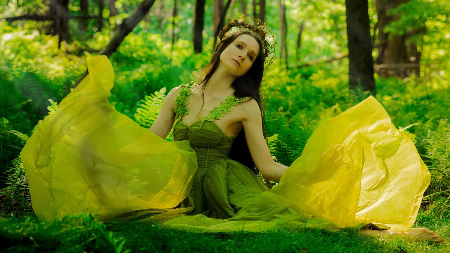 Woman in flowing yellow-green dress posing among lush forest ferns.