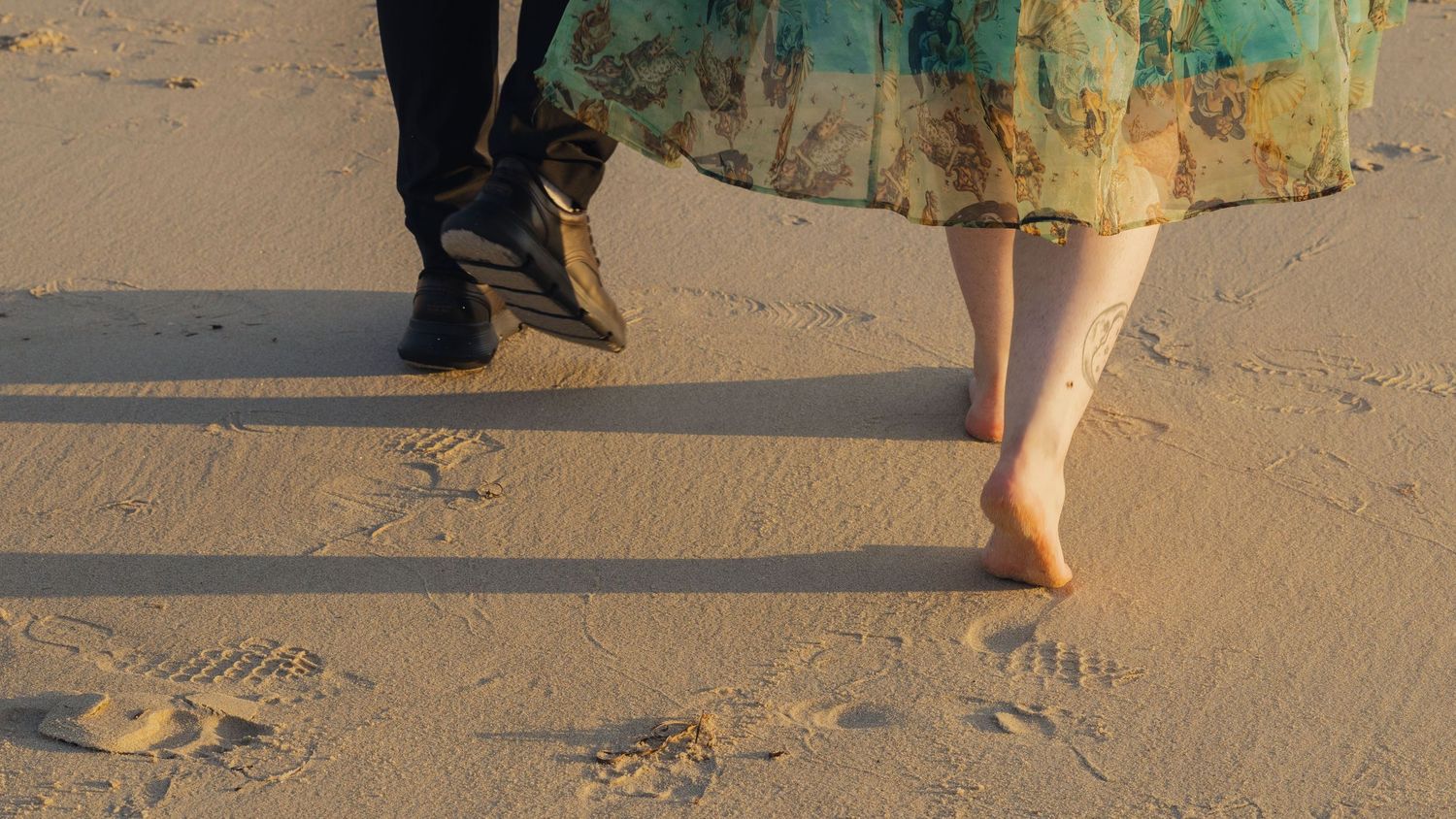 Close-up of feet walking on sandy beach during golden hour.