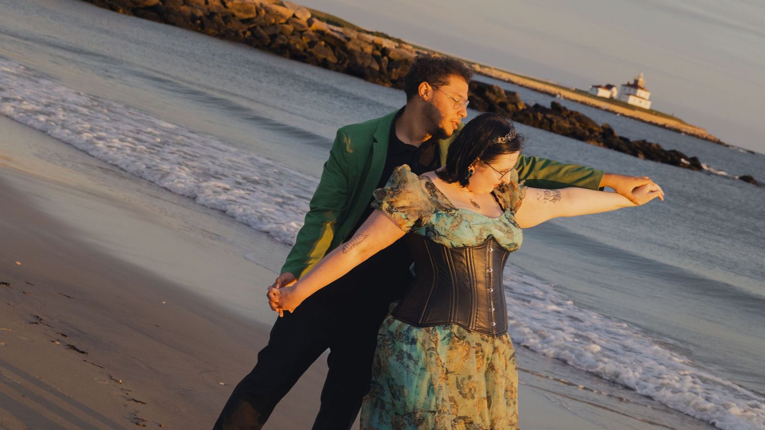 Couple dancing on beach at sunset with waves crashing in background.