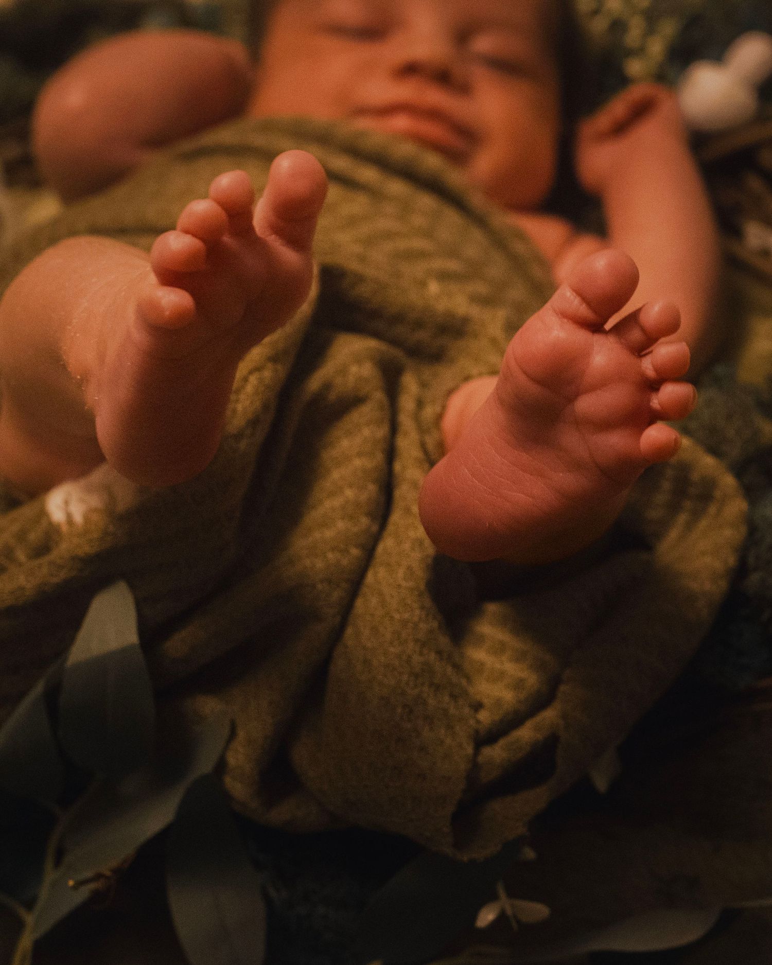 Close-up of tiny newborn baby toes wrapped in a soft brown blanket in warm lighting.