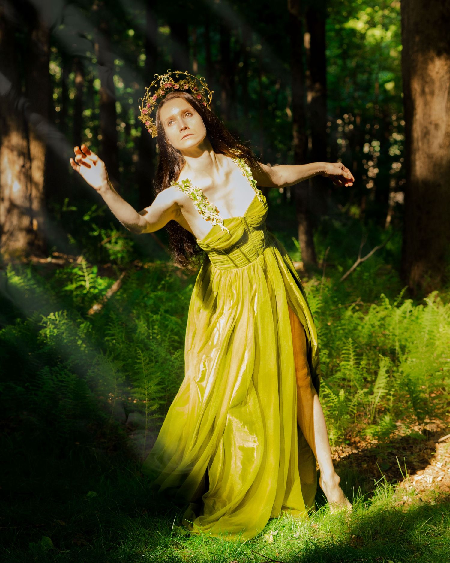 Woman in yellow-green dress and floral crown dancing in forest light.