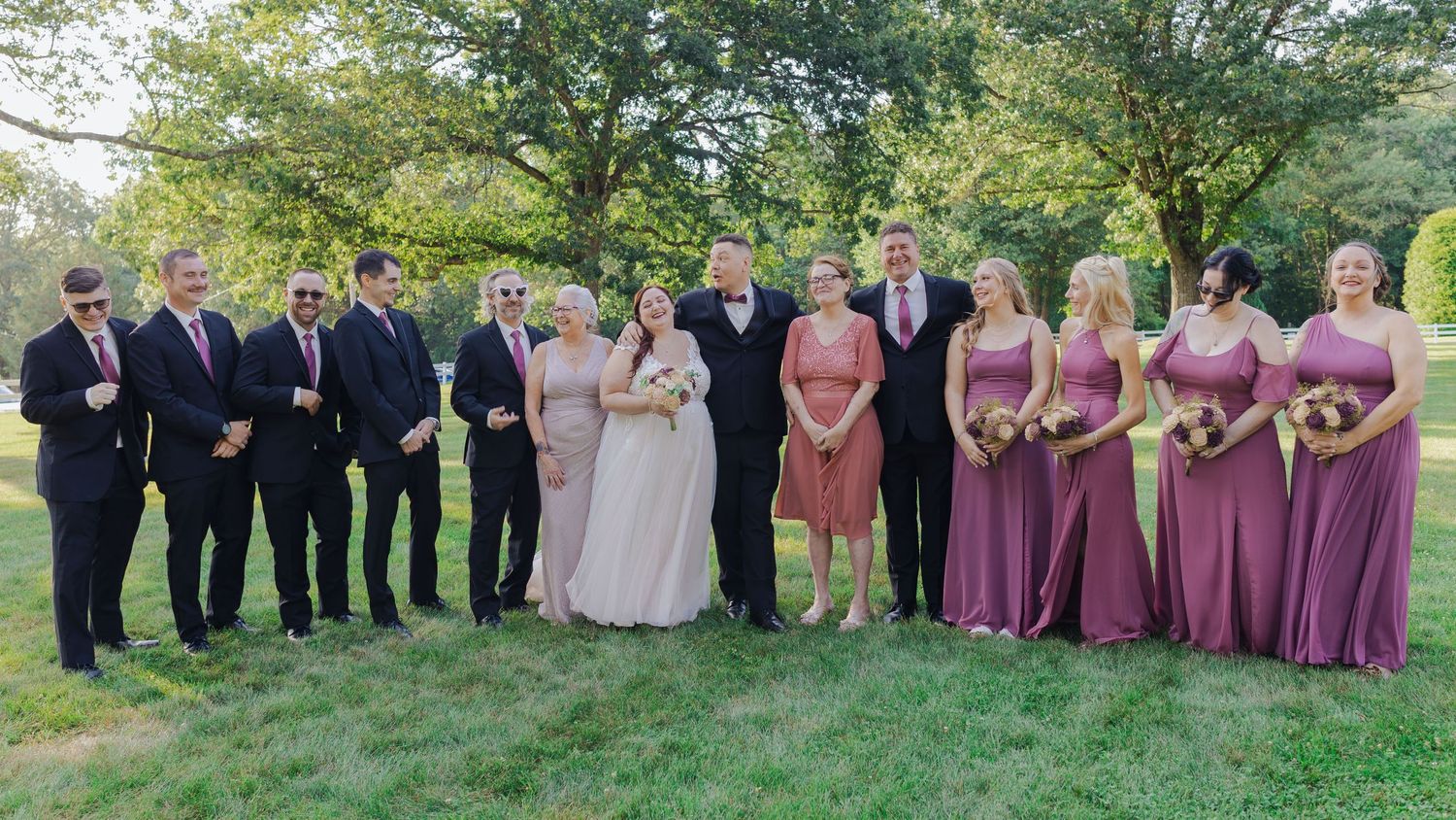 A wedding party poses outdoors in a line formation wearing pink and black formal attire.