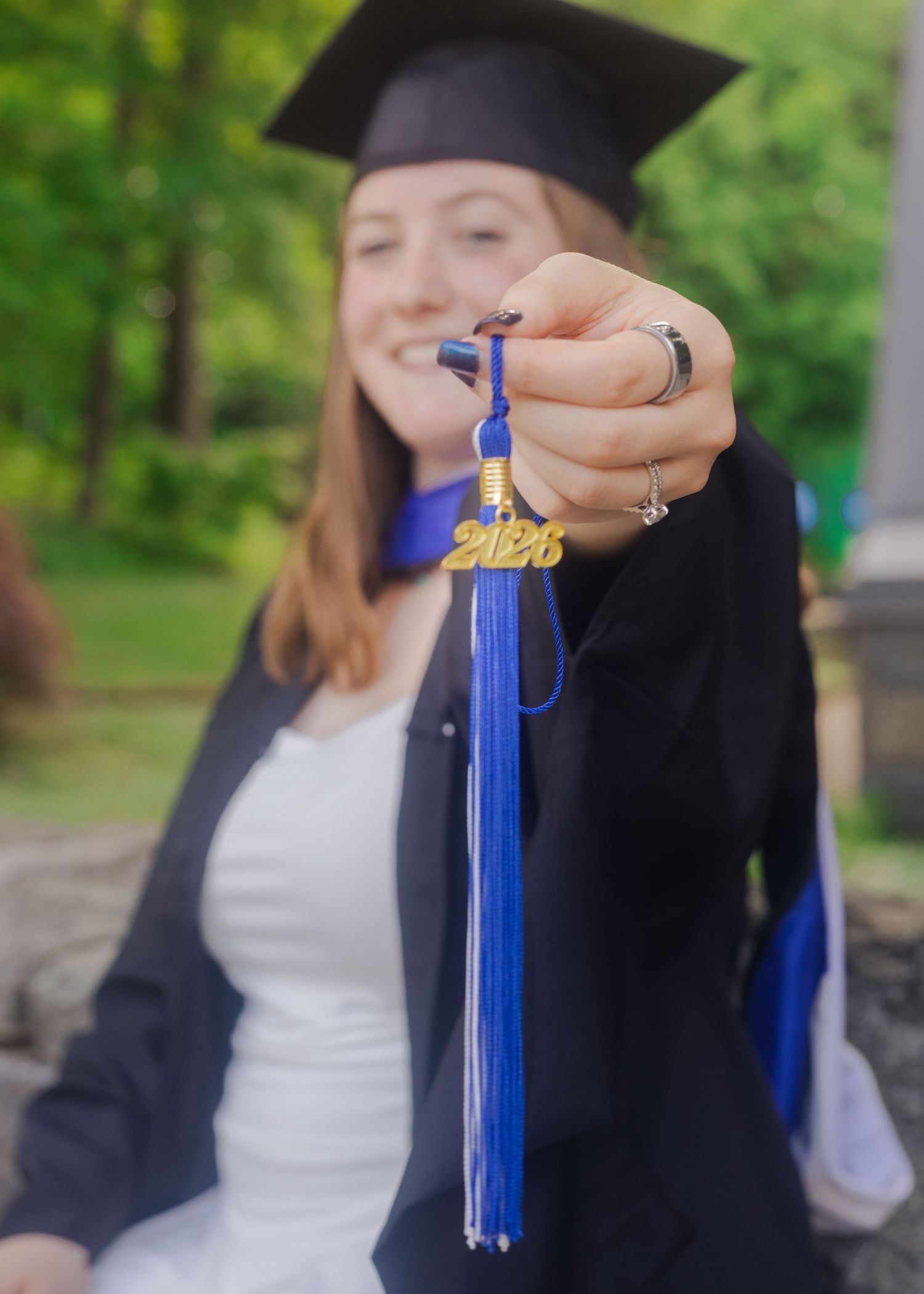 A graduate holds up a blue 2016 tassel toward the camera while wearing cap and gown.