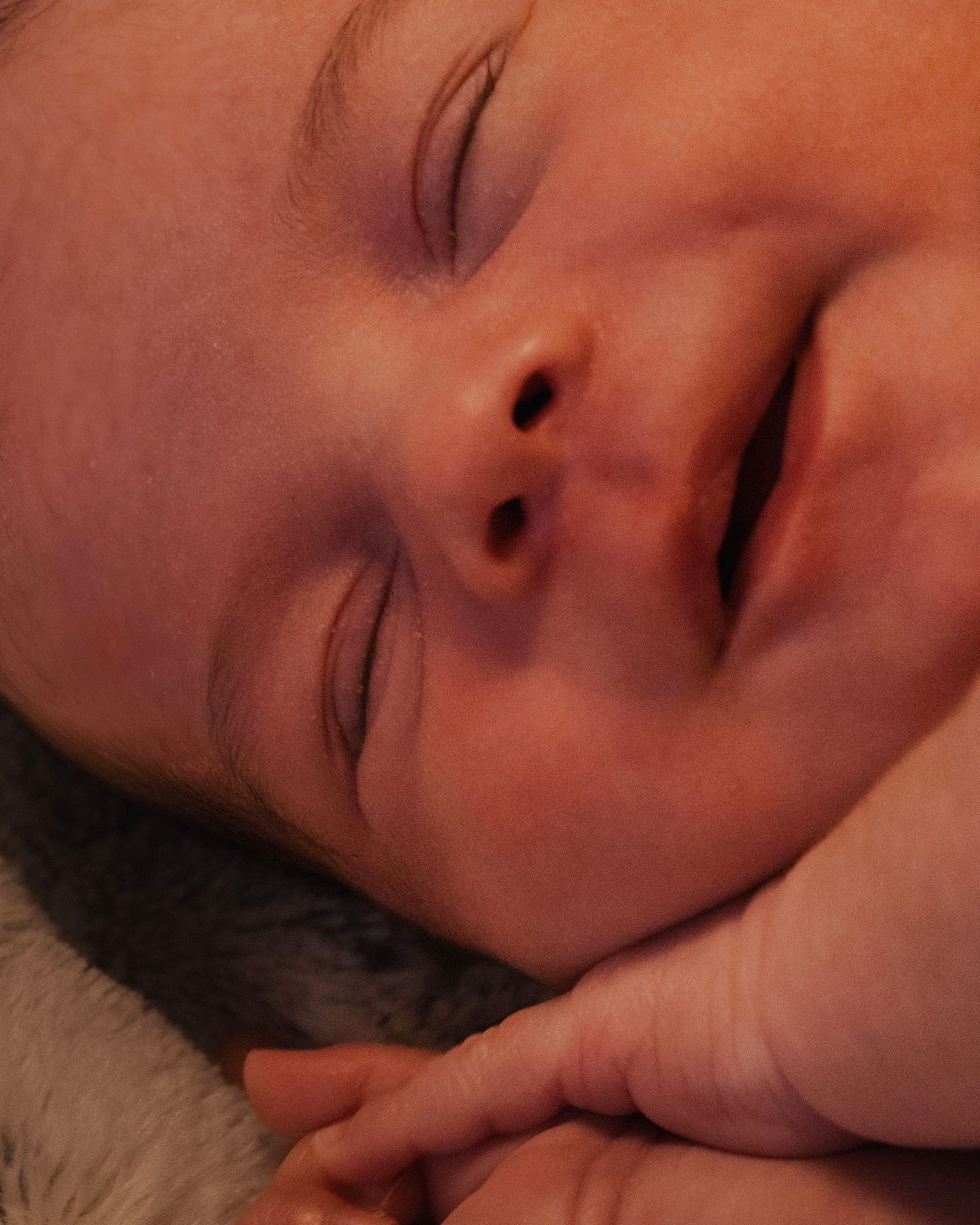 A sleeping infant rests peacefully with closed eyes and soft skin in warm lighting.
