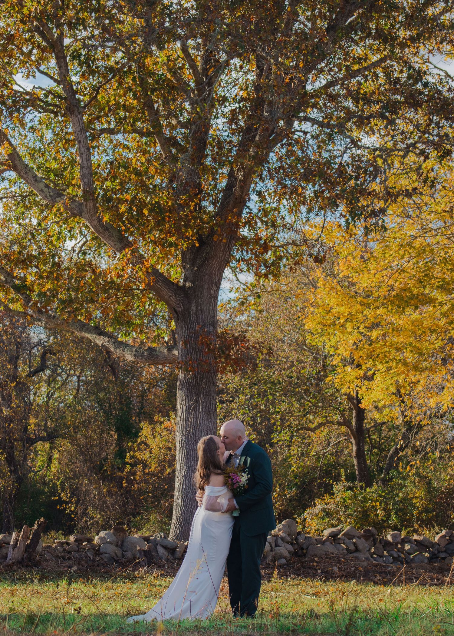 A couple shares a romantic moment under golden autumn trees during an outdoor wedding photoshoot.