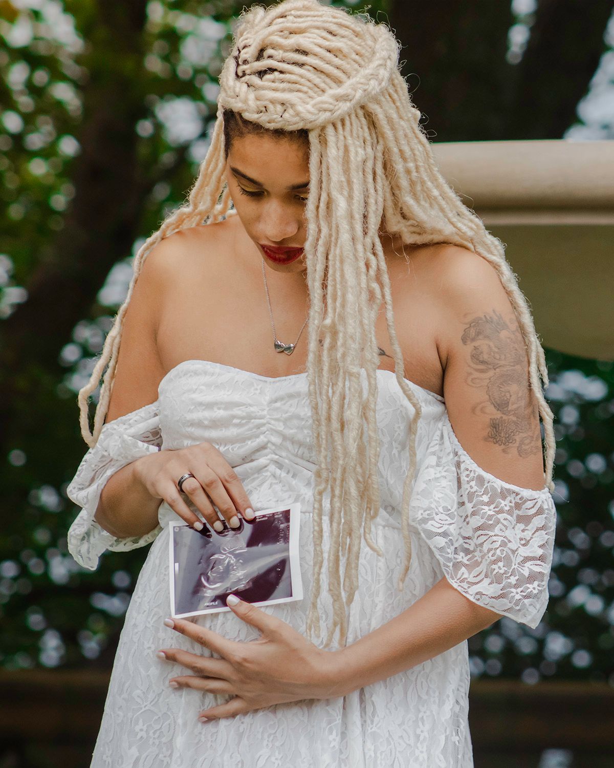 Intimate maternity portraits featuring a white lace dress in an outdoor setting.
