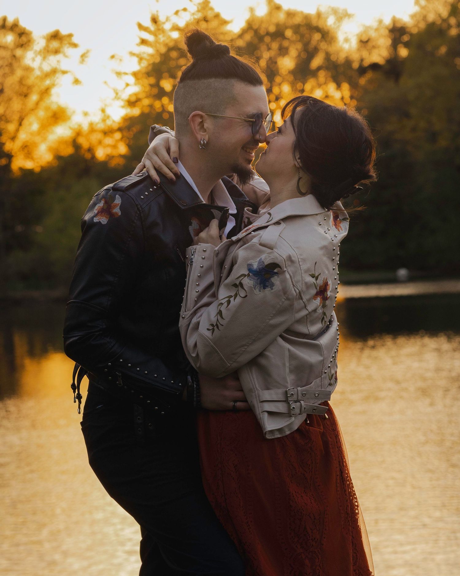 Couple sharing a romantic moment at golden hour by a reflective lake, wearing leather jackets.