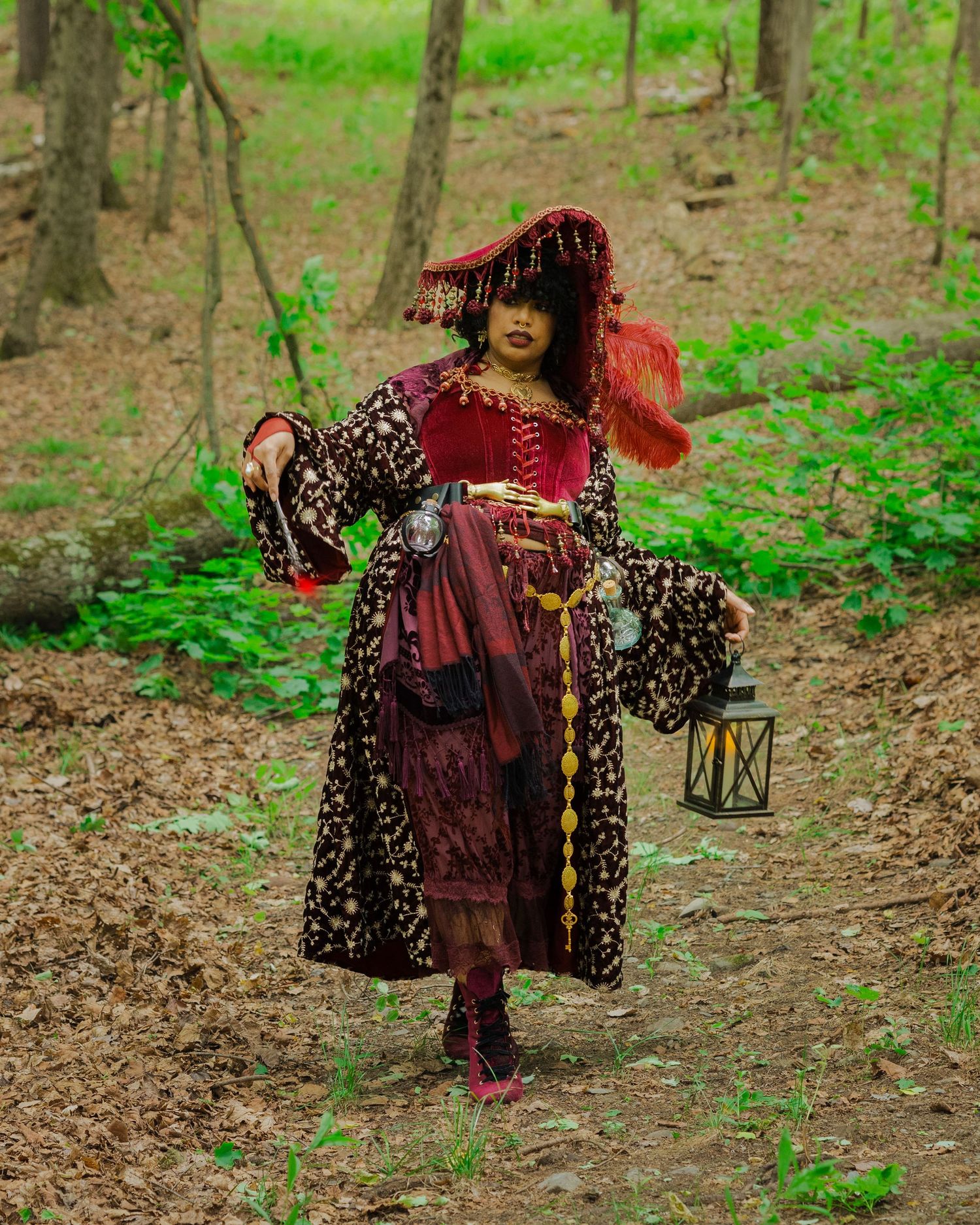 Woman in elaborate pirate costume with red hair, lantern, and forest backdrop.