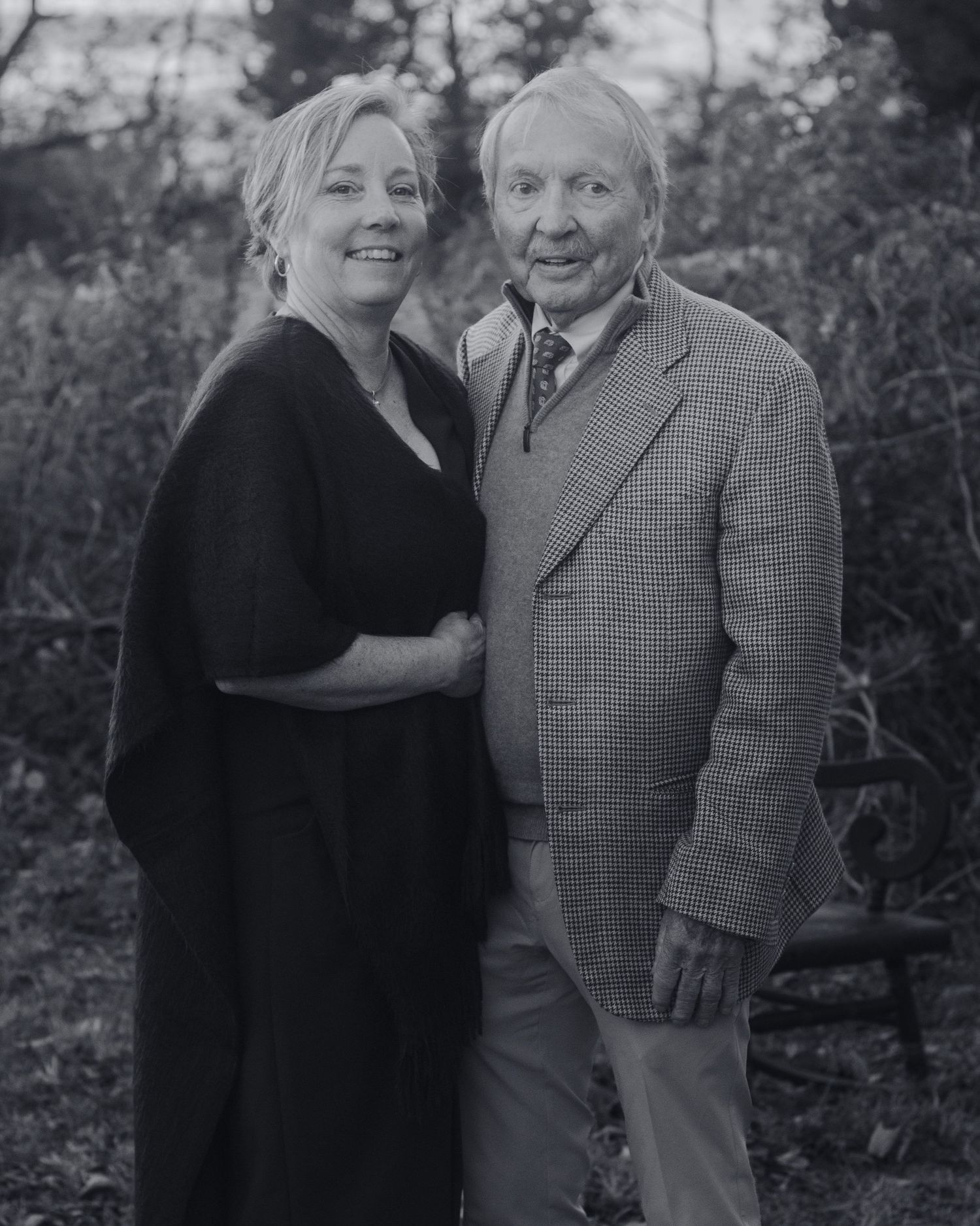 Black and white vintage portrait photograph showing two people embracing outdoors in a garden setting.