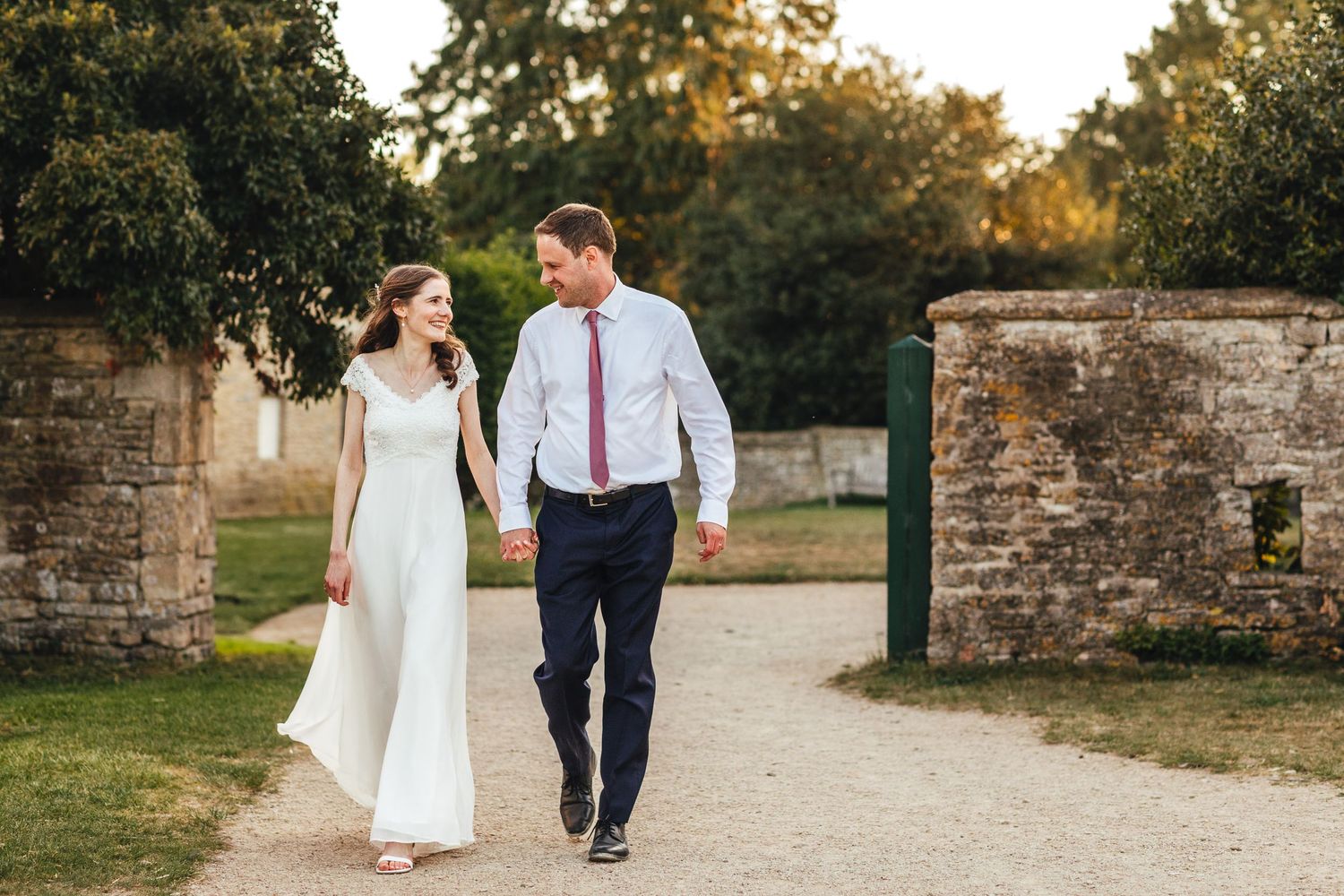 Bride and groom walking at sunset at Cogges Manor Farm, Oxfordshire barn wedding photography