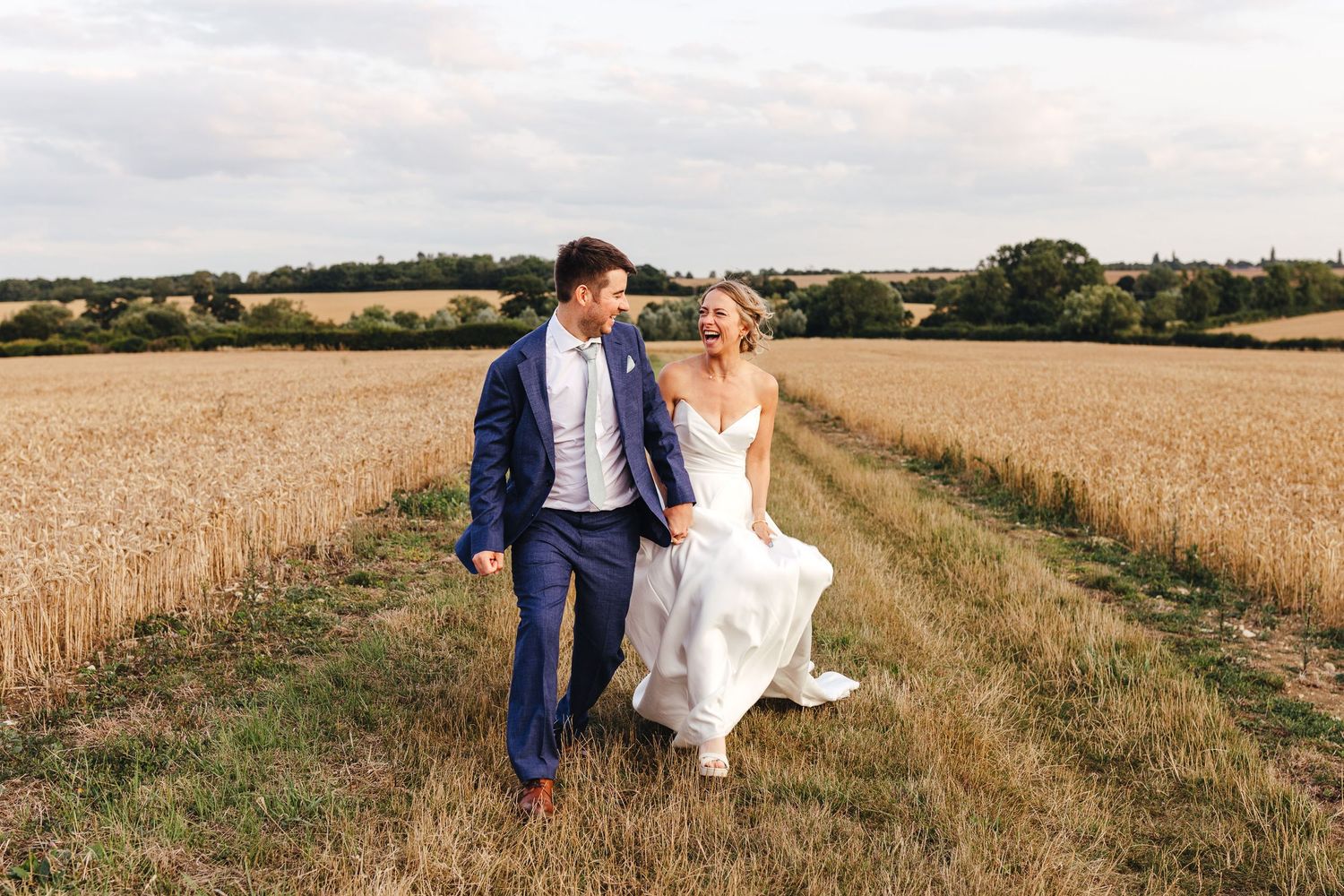Bride and groom walking through fields at Huntsmill Farm barn wedding in Buckinghamshire, relaxed documentary wedding photography