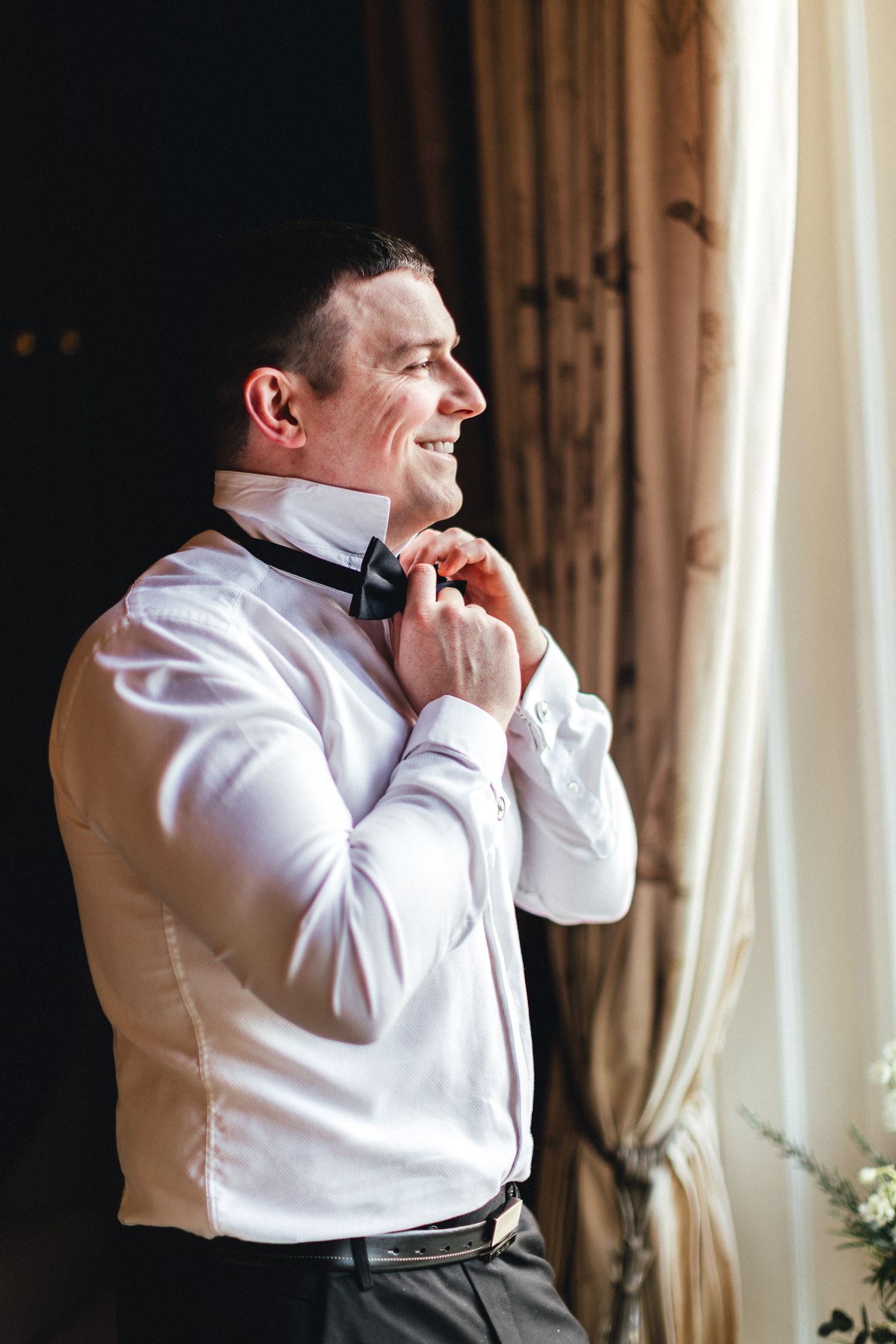 Groom adjusting tie by window at Falcon Manor Settle, elegant country house wedding photography in North Yorkshire