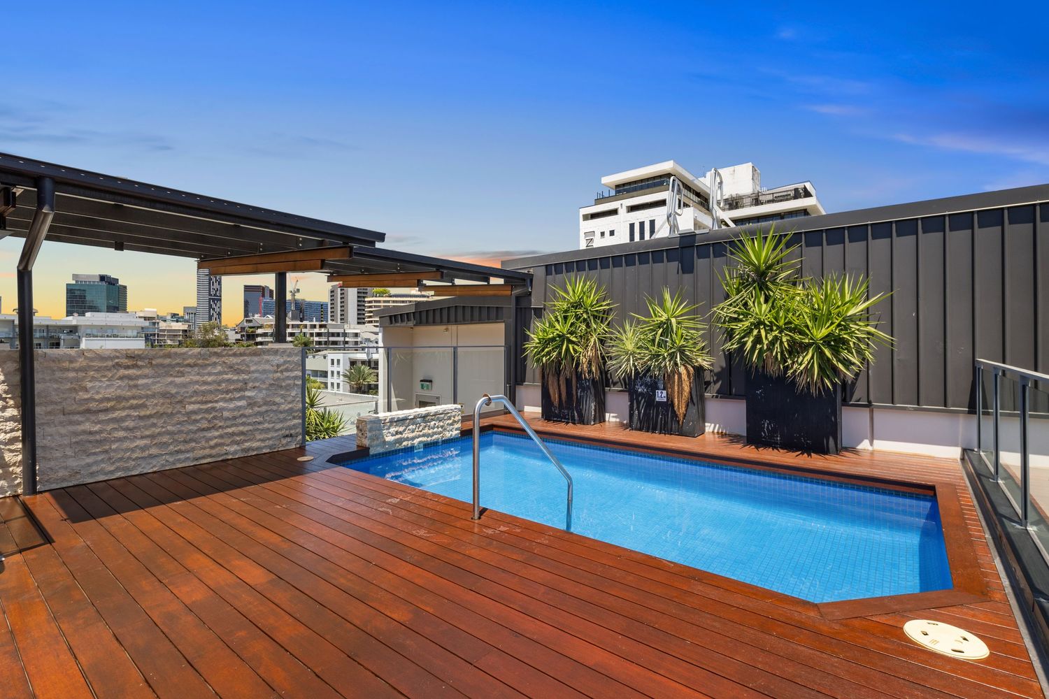 Rooftop deck with wooden flooring and swimming pool overlooking urban buildings.