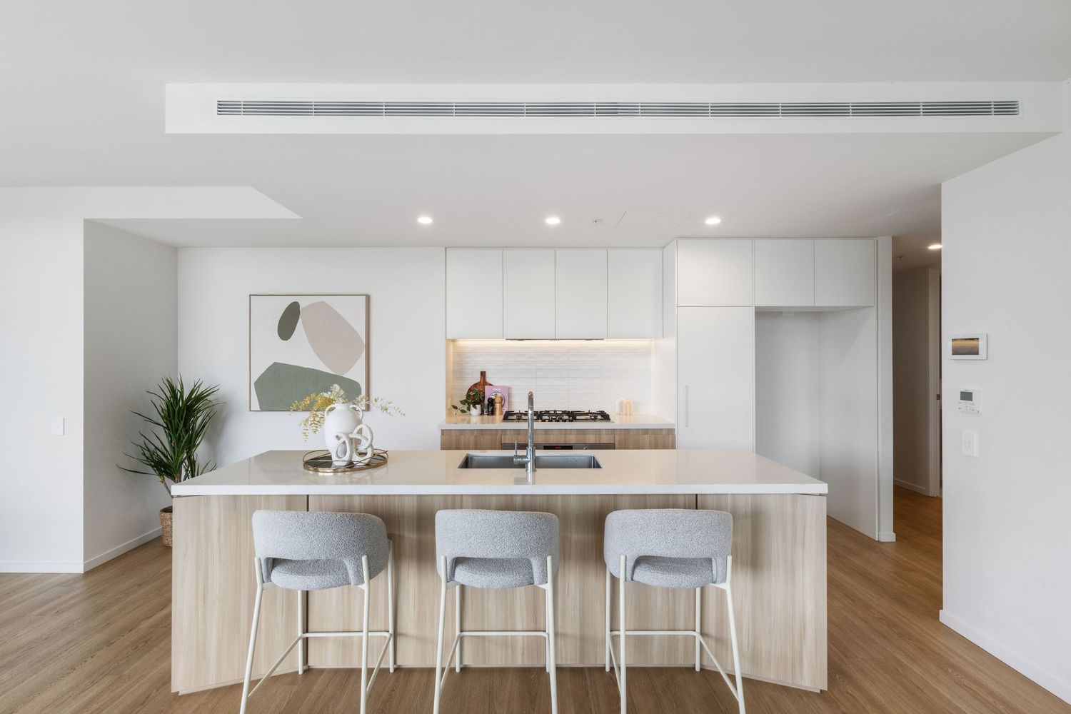 Modern open concept apartment interior with minimalist white kitchen and wood flooring.