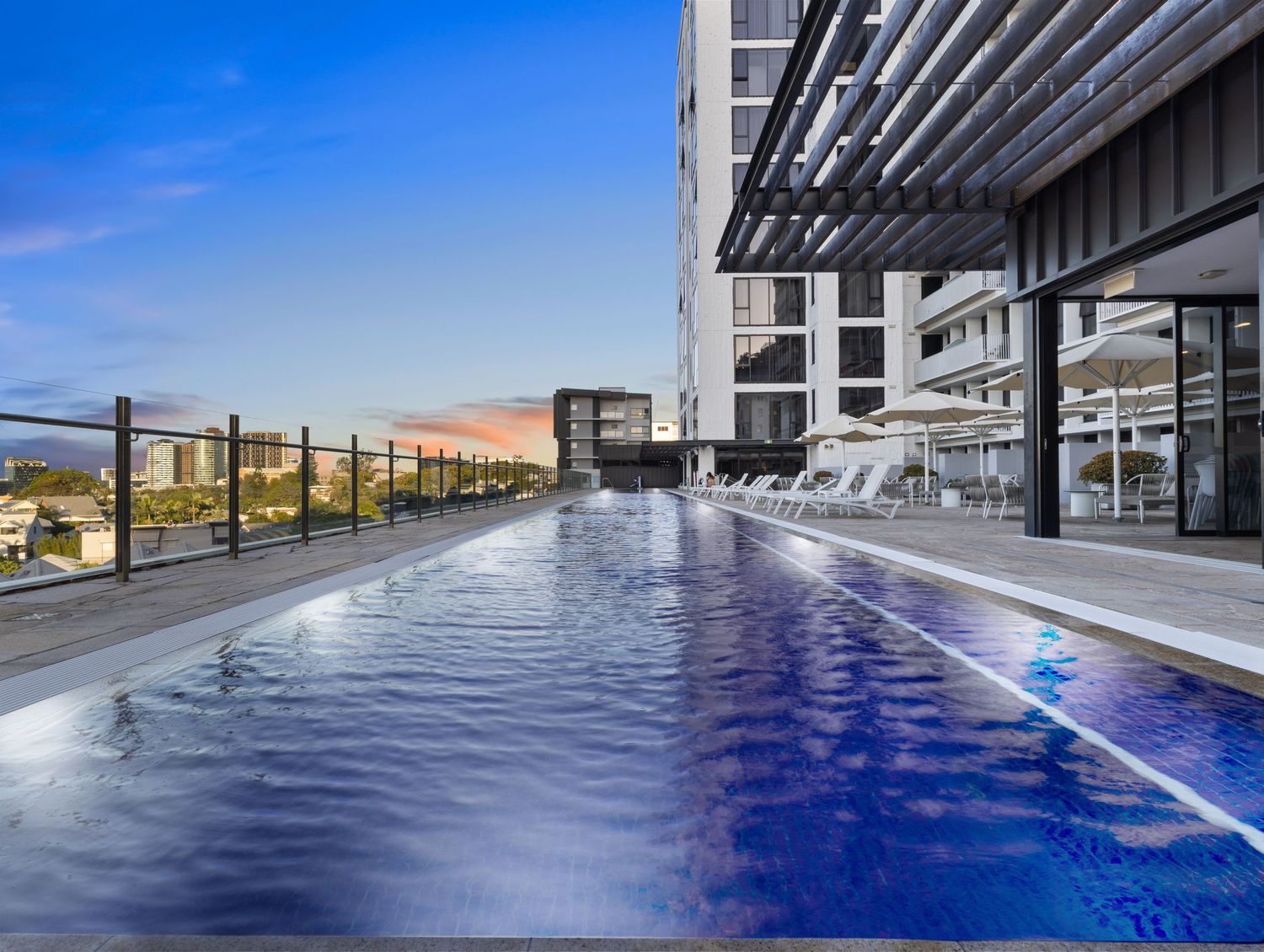 Sleek infinity pool with geometric lines and glass barriers reflecting sky and clouds.