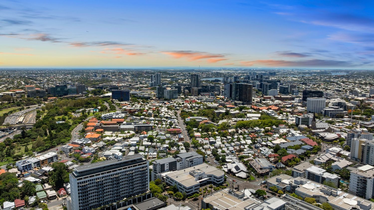 Sweeping aerial view of Brisbane's central business district and surrounding suburbs under blue skies.