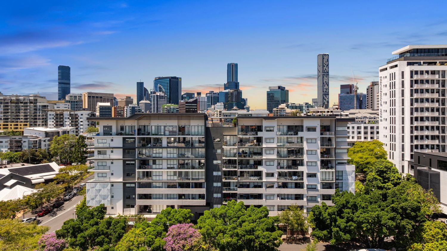 Panoramic cityscape view of Brisbane's modern skyline with high-rise buildings against a bright blue sky.