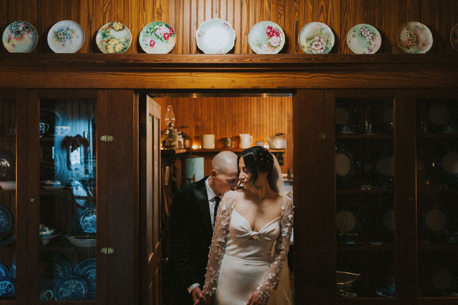 Couple shares intimate moment in a cozy interior space decorated with decorative plates on wooden shelf above.