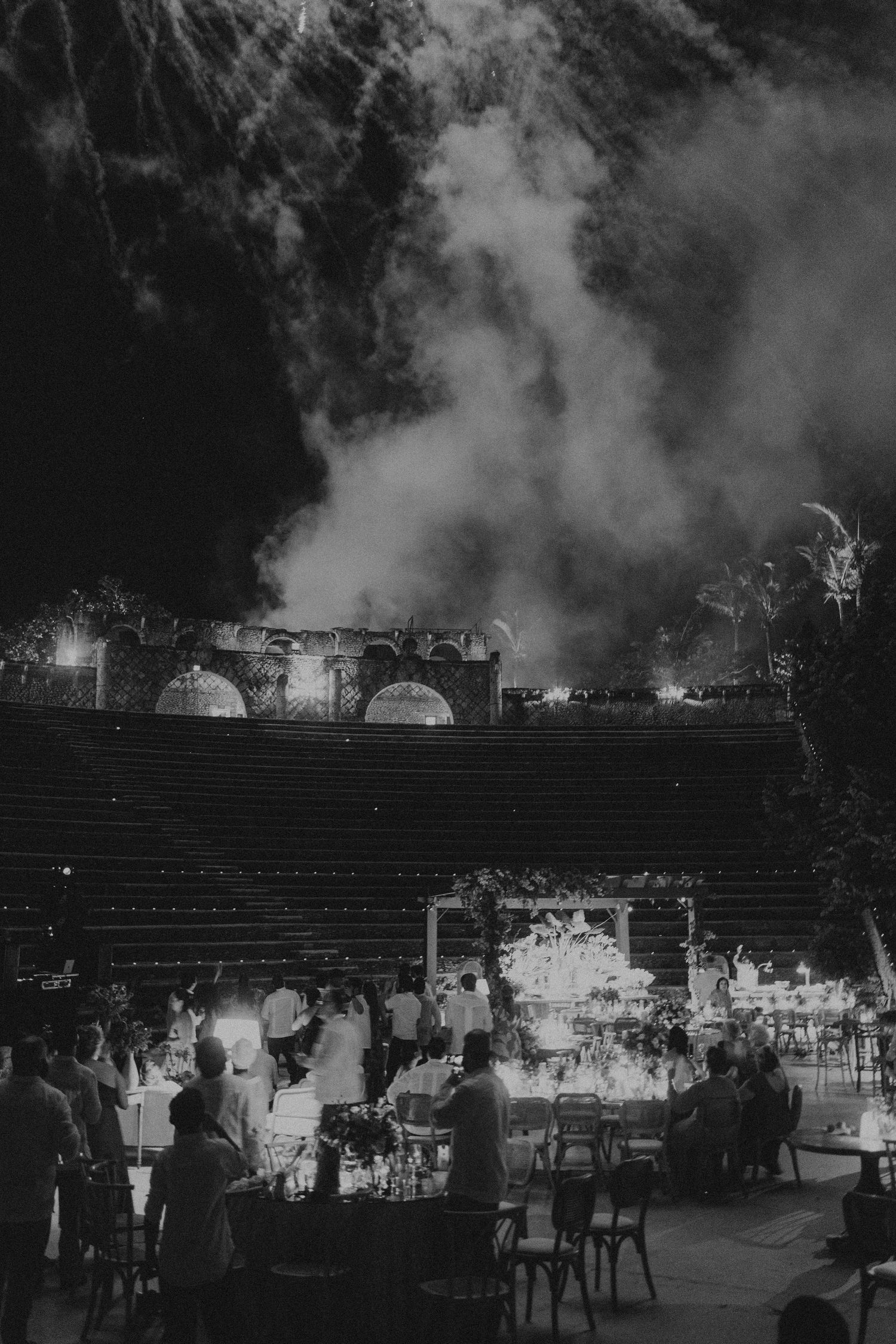 An evening outdoor wedding reception with string lights and dramatic smoke effects.